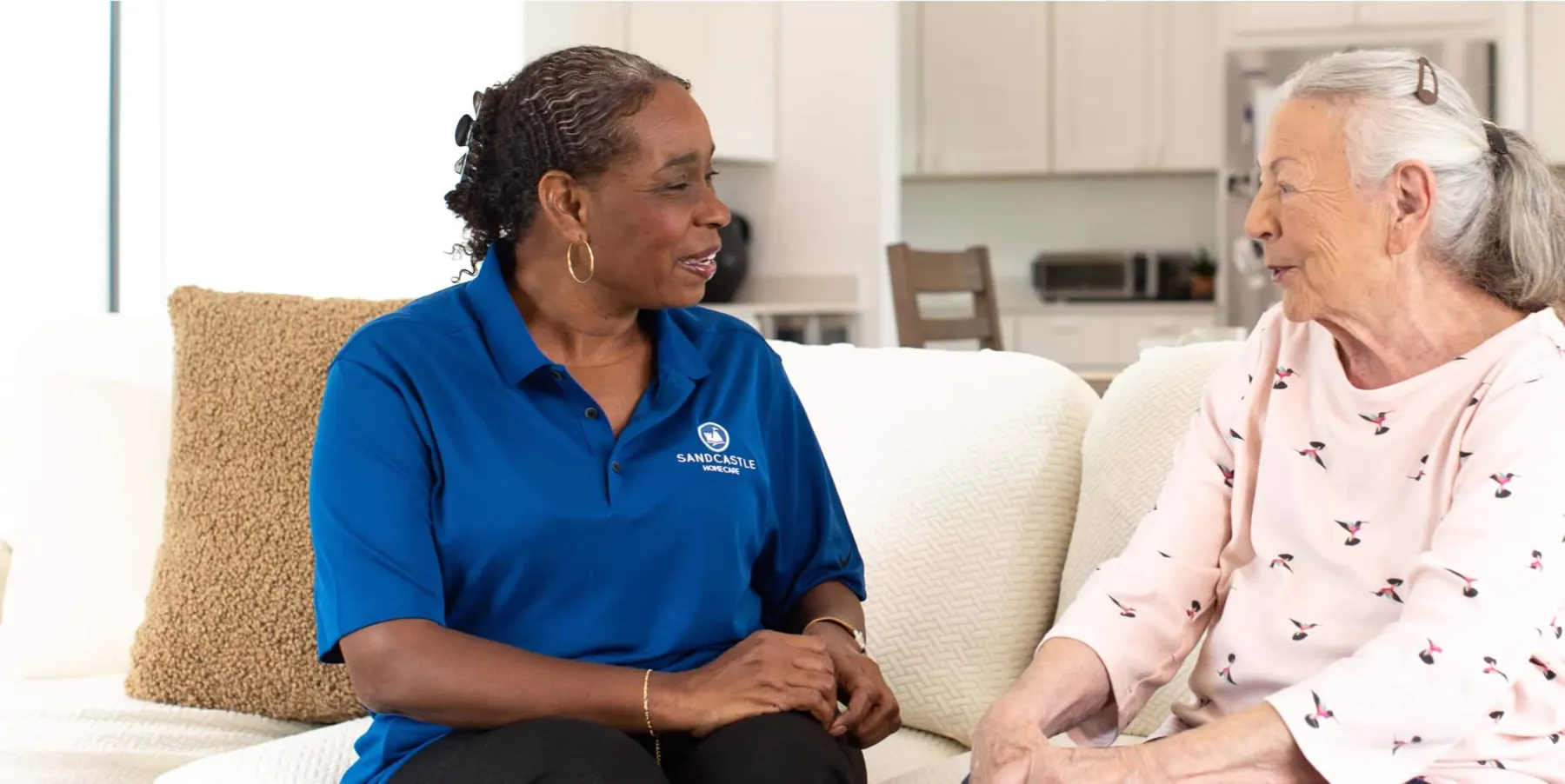 A Sandcastle Home Care caregiver talking with an older woman on her sofa