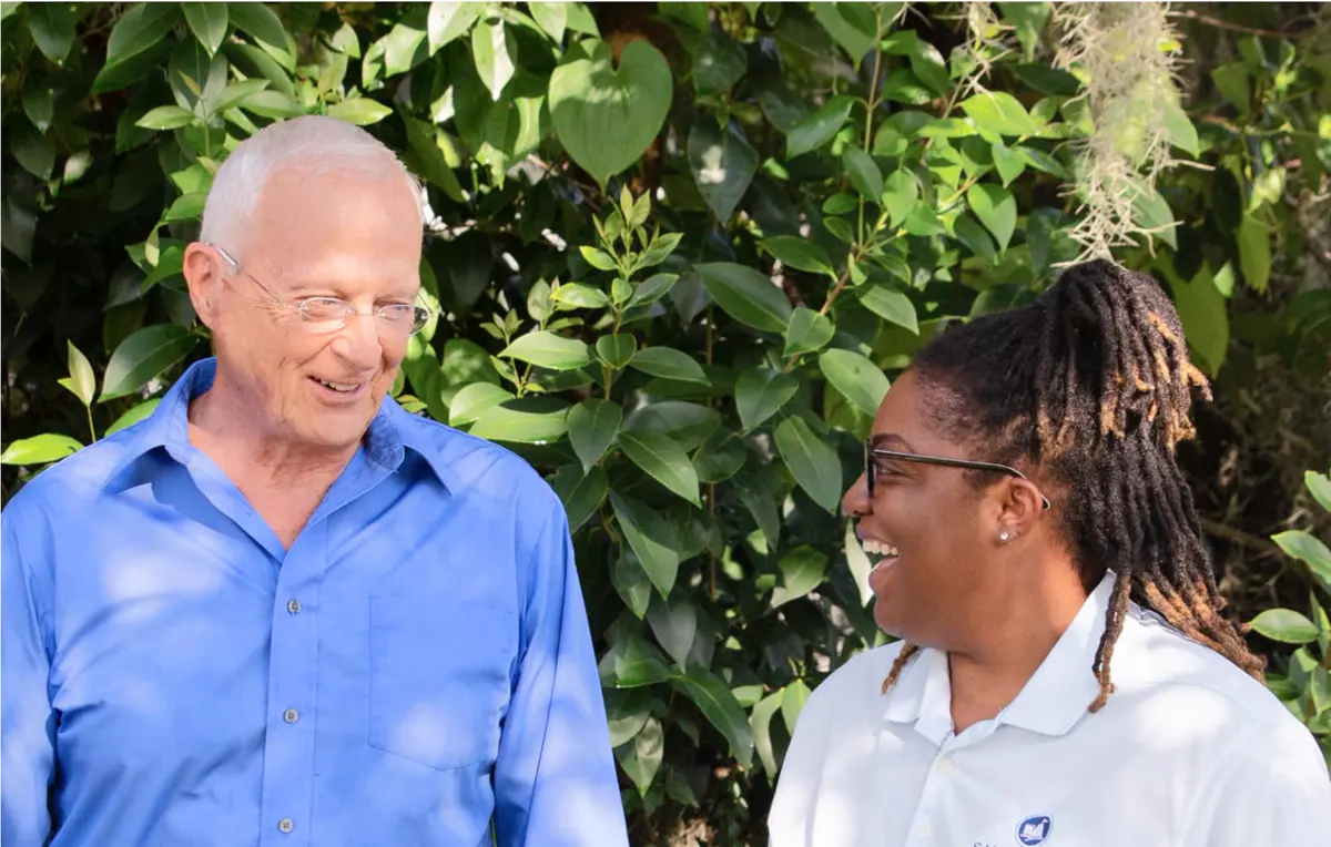 A caregiver and an older man laughing in a garden