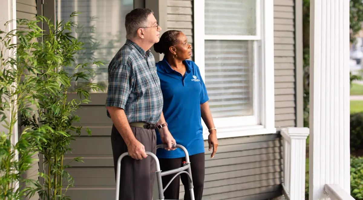 A caregiver beside a man with a walker on his front porch