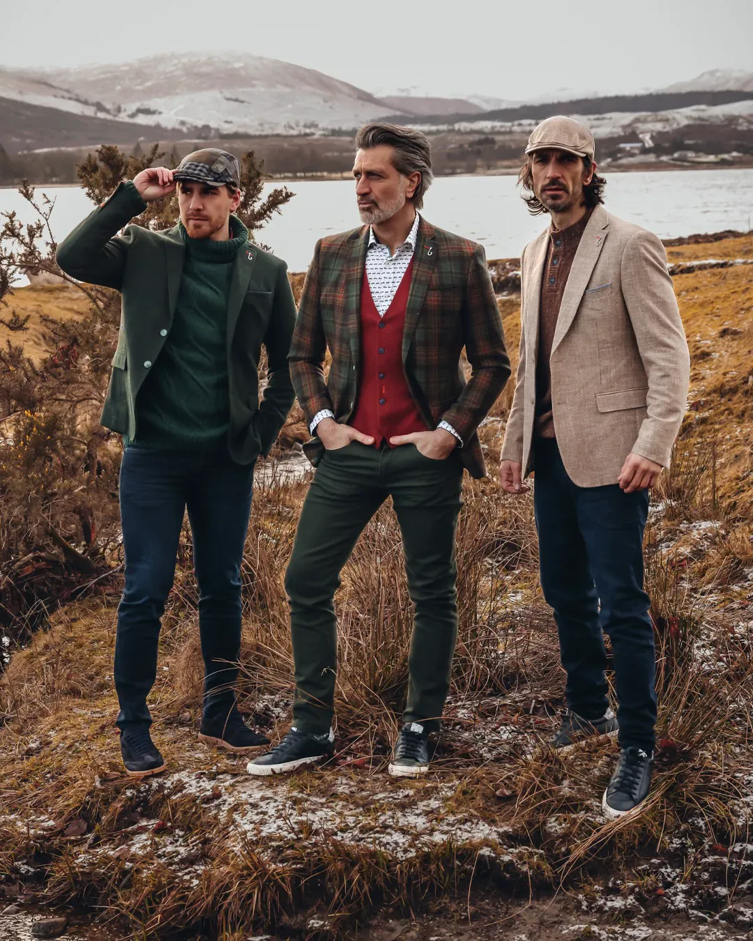 Three men in tweed jackets and flat caps on a winter hillside by a loch