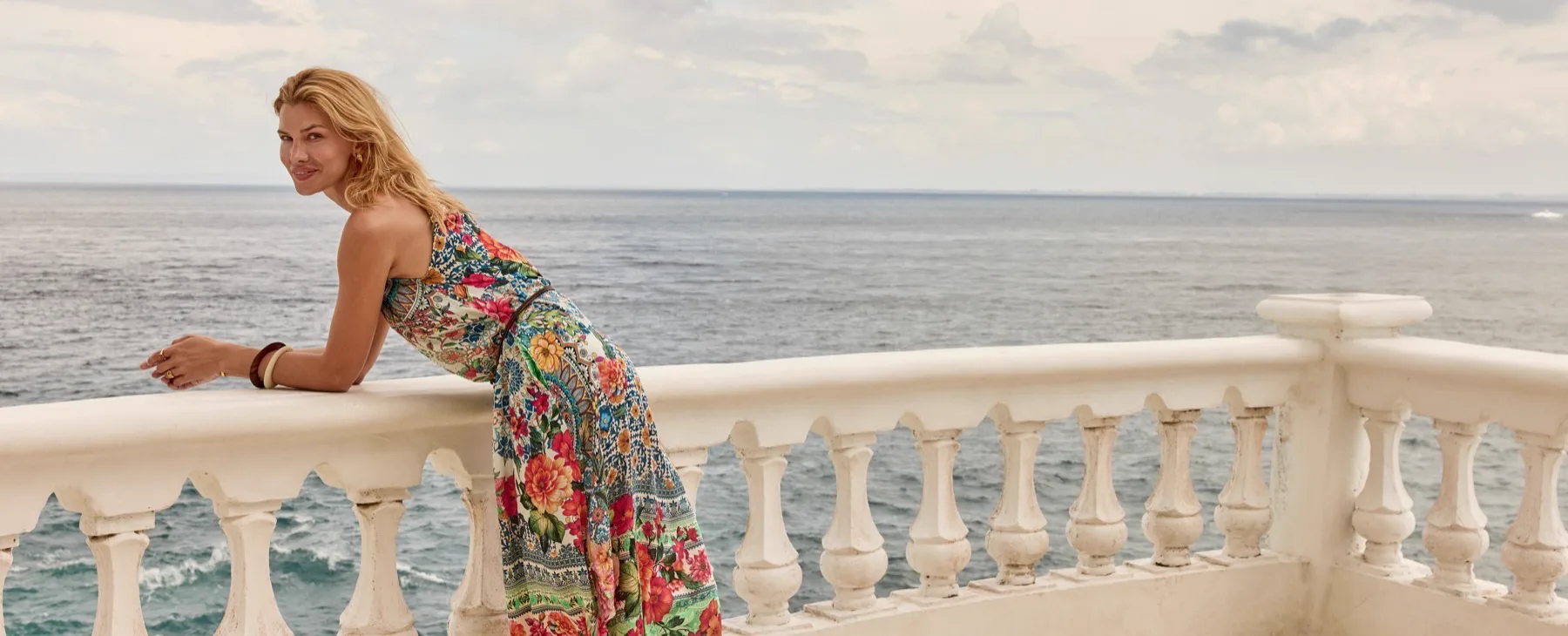 A woman in a Lula Soul floral maxi dress on a balcony above the sea