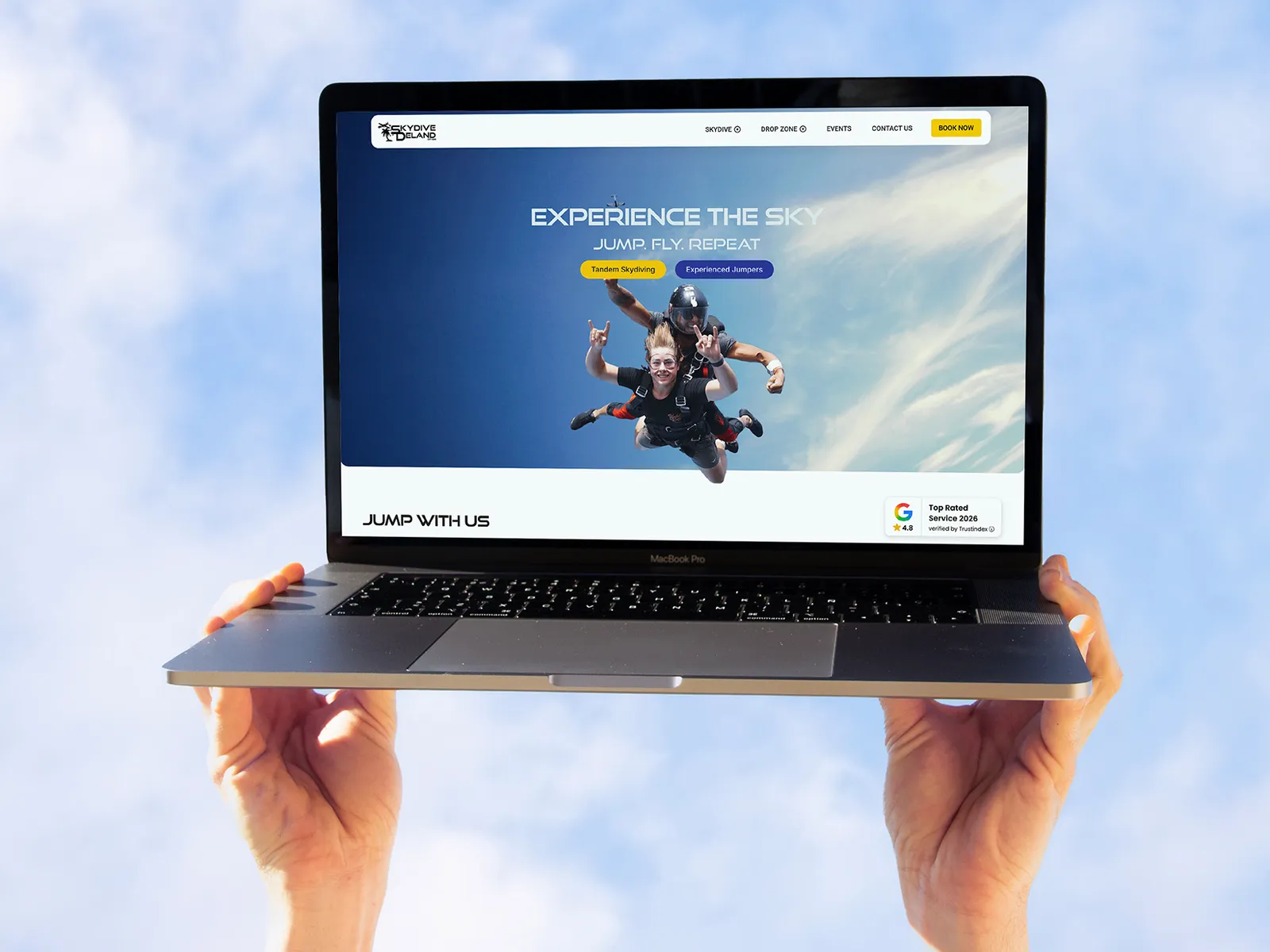 Skydive DeLand's homepage on a laptop held up to the sky, with Book Now at the top