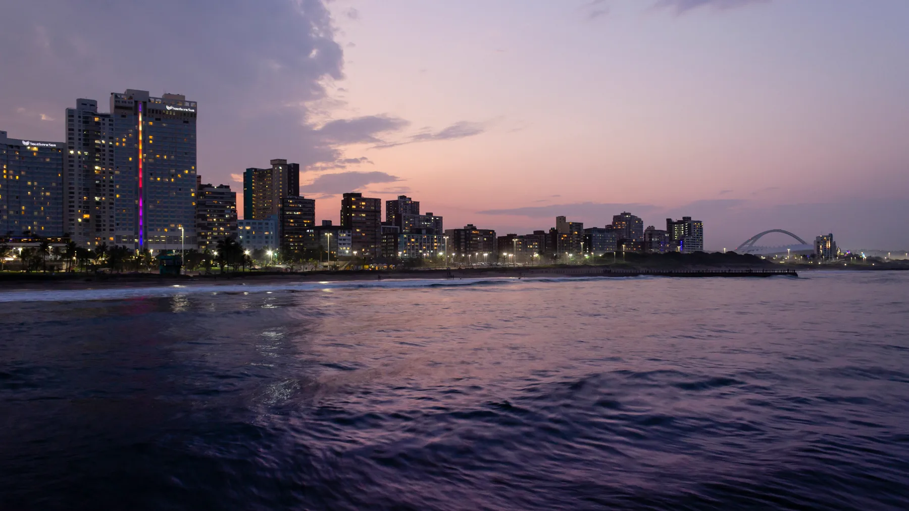 Durban's beachfront at dusk: the hotels and flats lit up along the shore, and the stadium arch in the distance