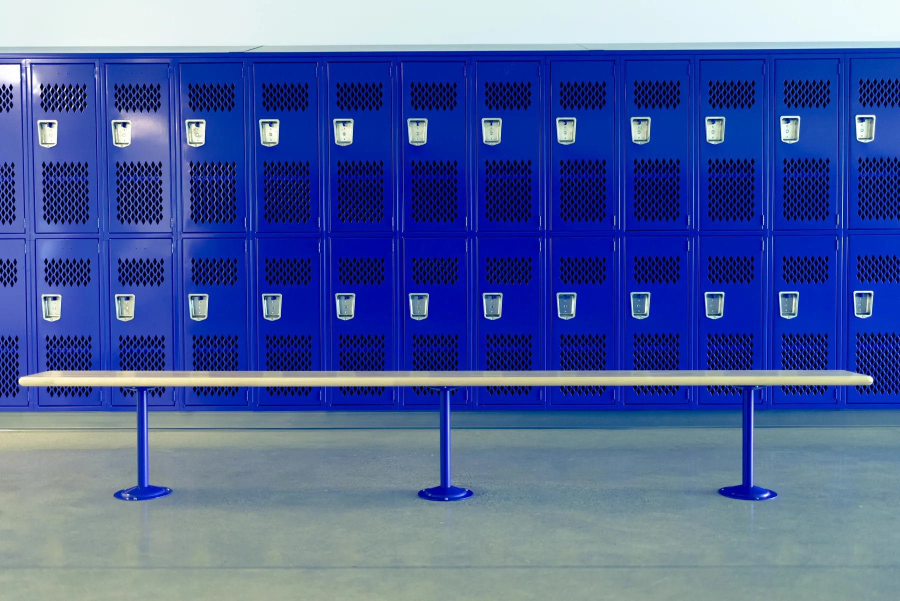 A row of blue ventilated steel lockers by Triple H Display, with a bench in front